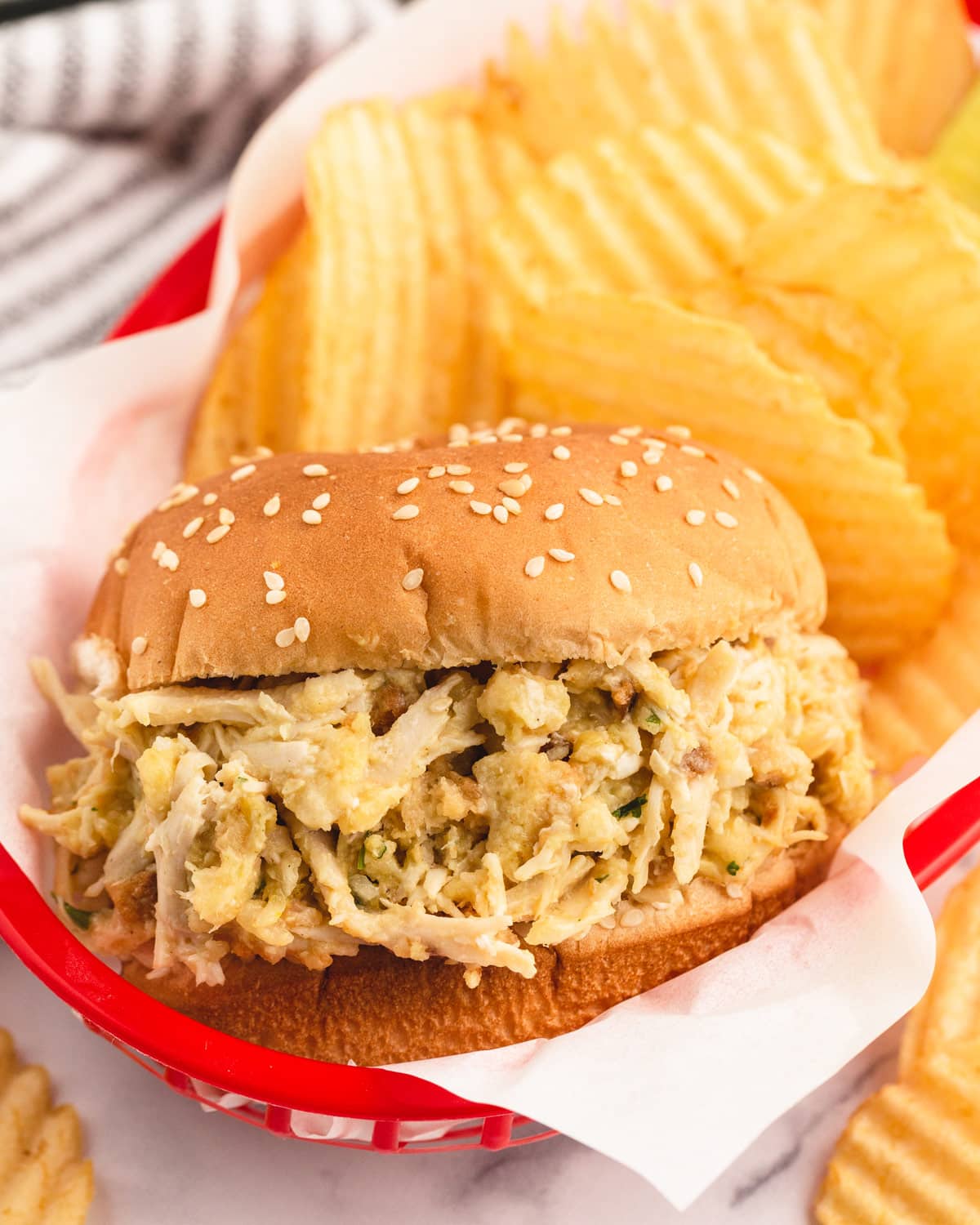 a shredded chicken sandwich in a basket with chips