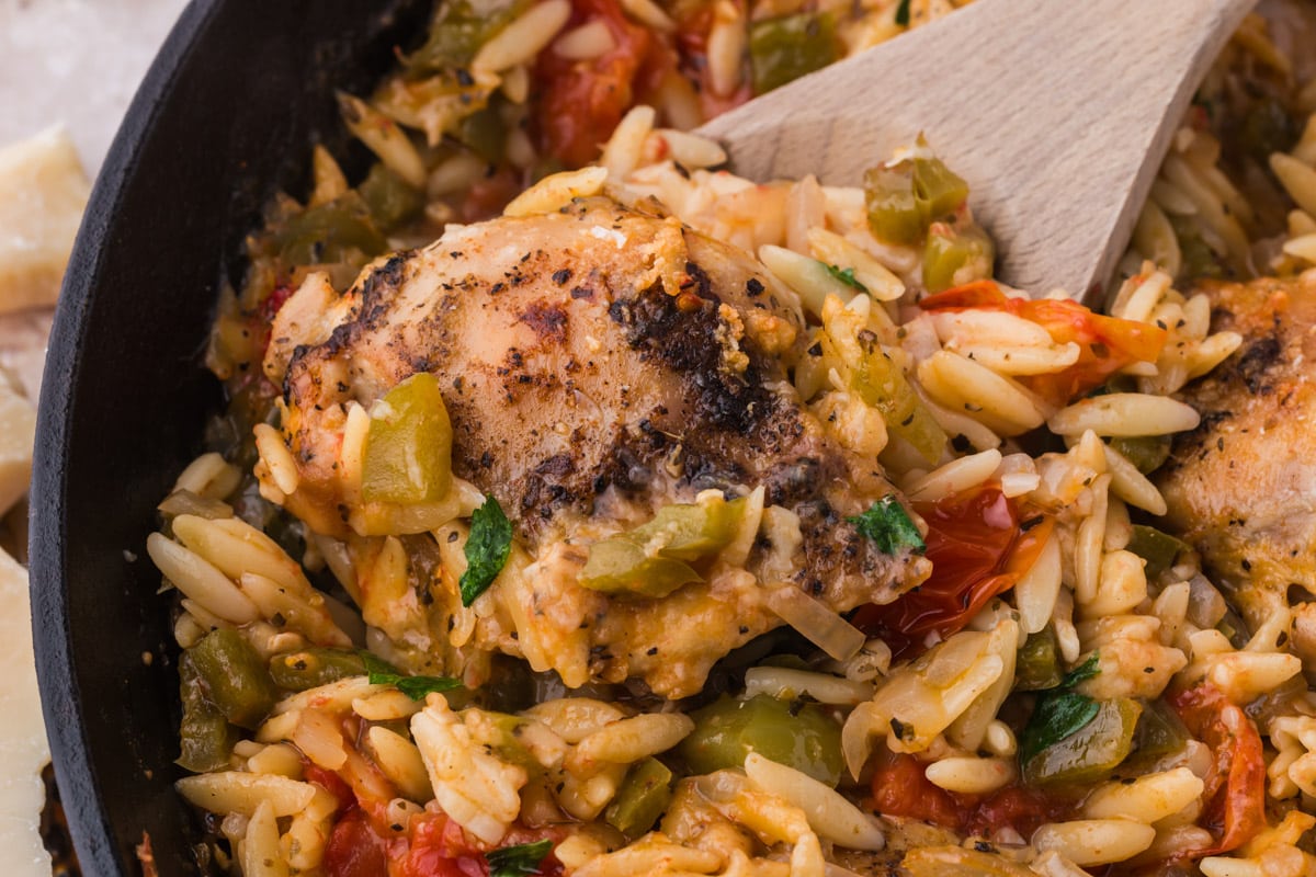 closeup of a piece of chicken with orzo in a skillet