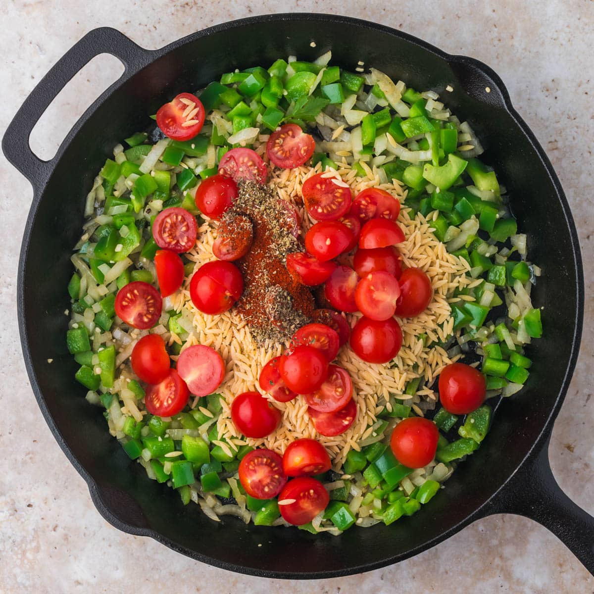 vegetables, orzo, seasonings and tomatoes in a skillet
