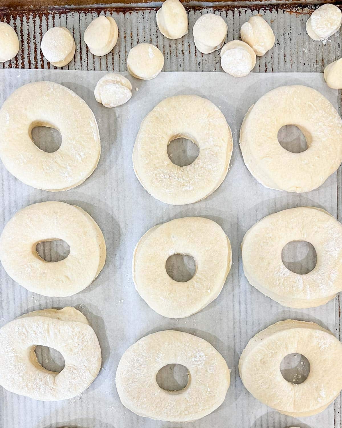 unbaked donuts cut on a baking sheet with donut holes at the top of the pan