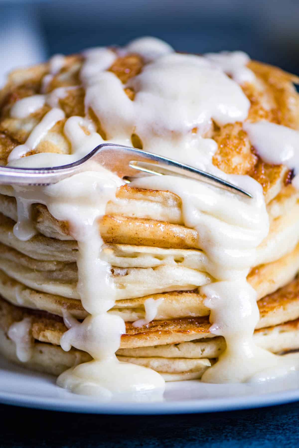 a fork cutting into a stack of glazed cinnamon roll pancakes