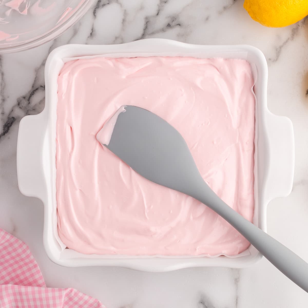 a spatula spreading pink lemonade filling in a baking pan