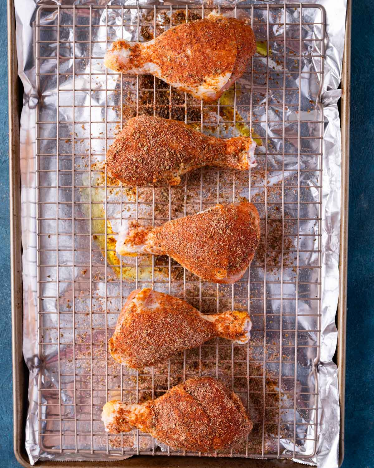 unbaked chicken legs with seasoning on a wire rack