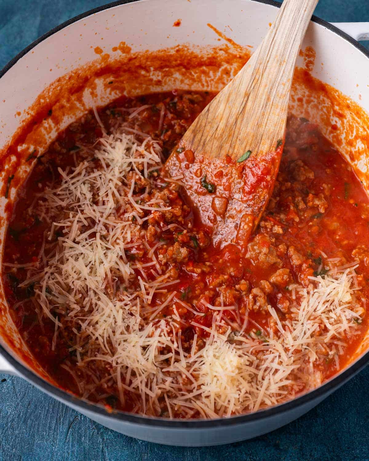 parmesan cheese shredded on top of spaghetti sauce in a pan