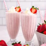 two strawberry milkshakes sitting on a table with straws