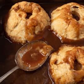 closeup of amish apple dumplings in a pan with a spoon in caramel sauce
