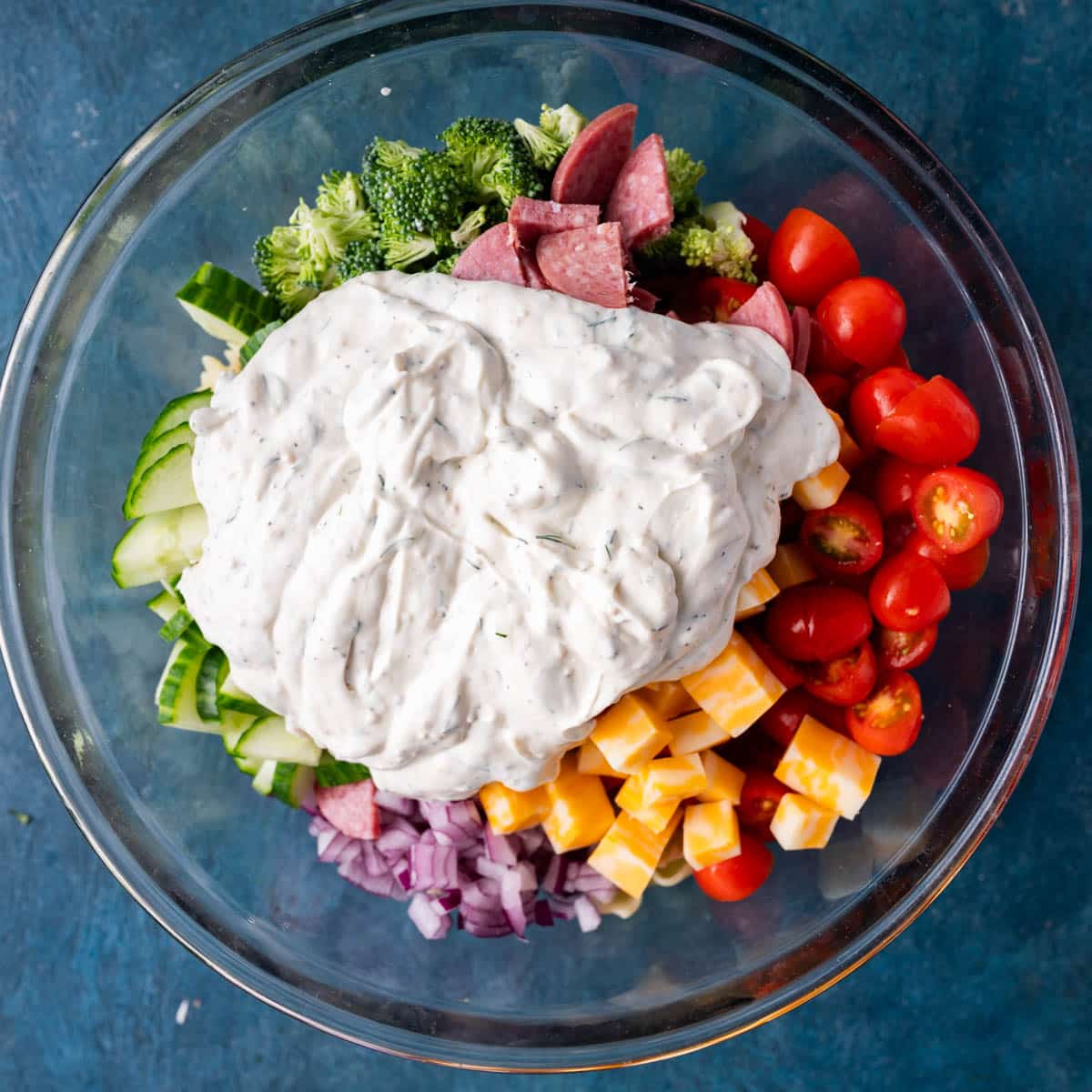 veggies, meat and cheese in a bowl with a white dressing on top, unmixed