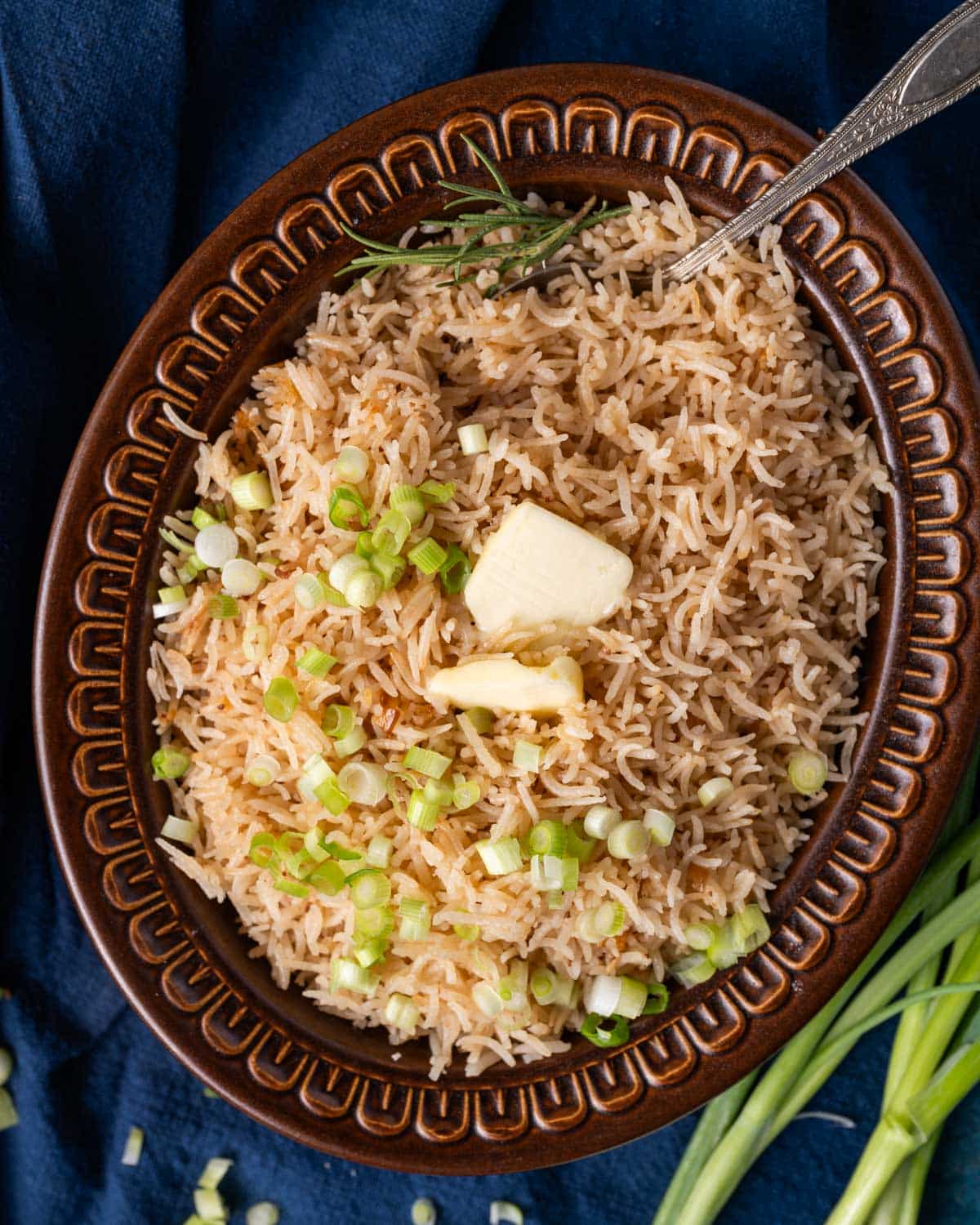 fluffy butter rice in a bowl with butter on top and fresh herbs