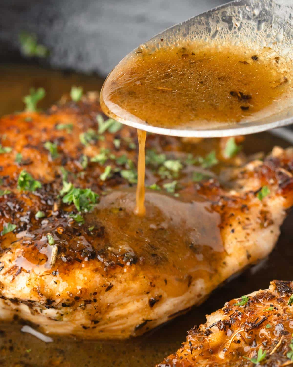 Spooning garlic herb butter sauce over chicken breasts