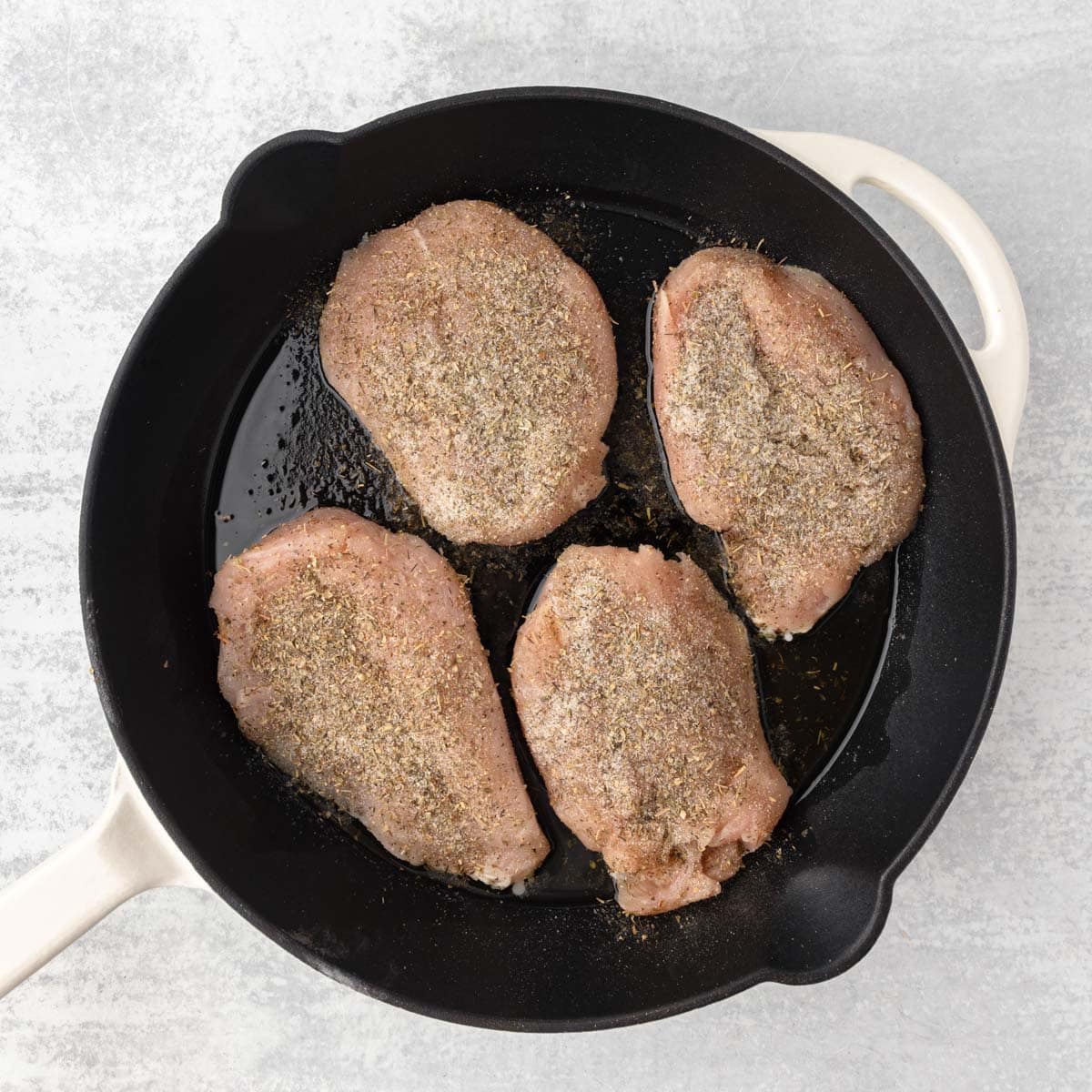 4 uncooked chicken breasts in a skillet