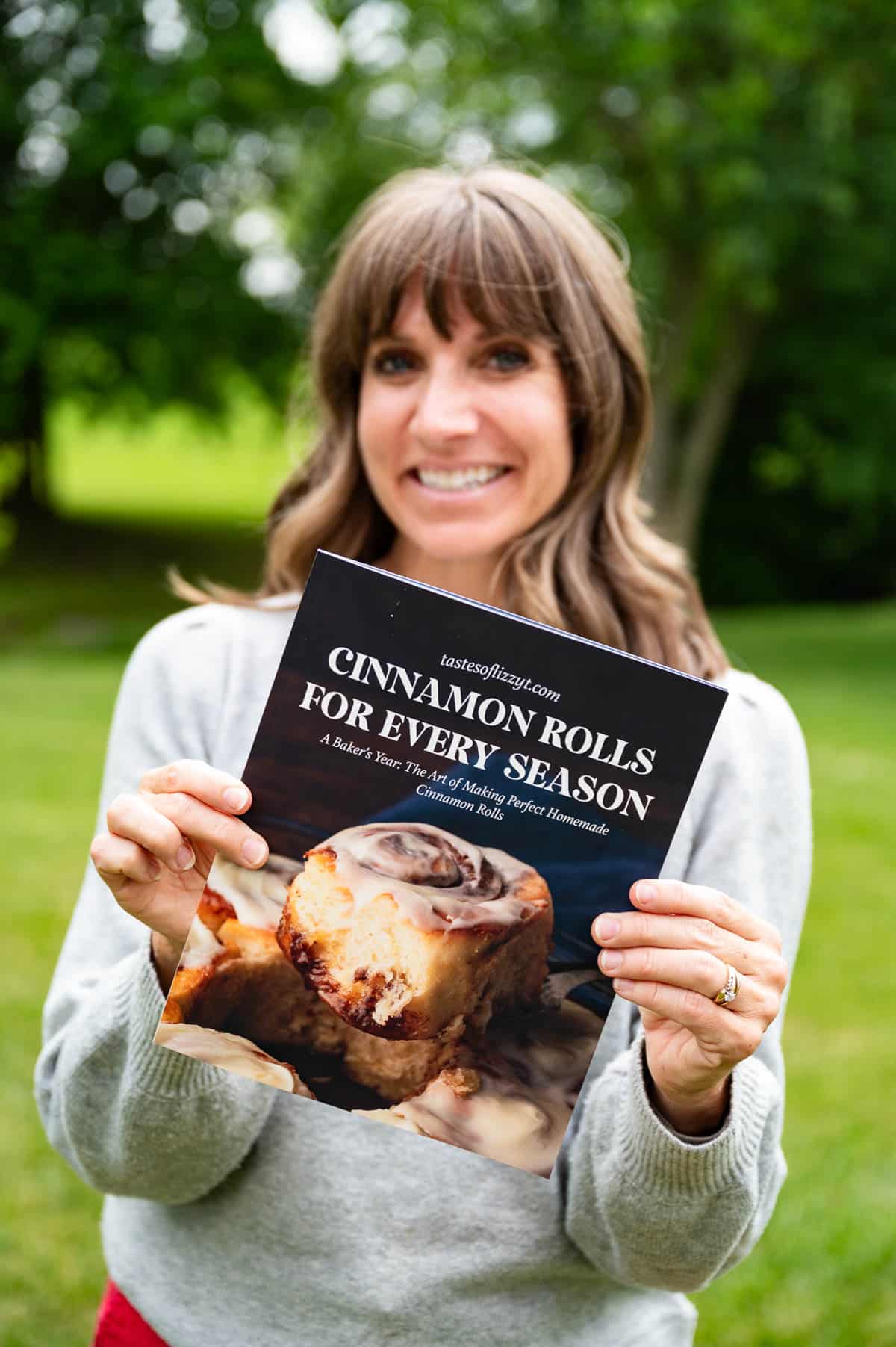 Julie from tastes of lizzy t holding a cinnamon roll cookbook