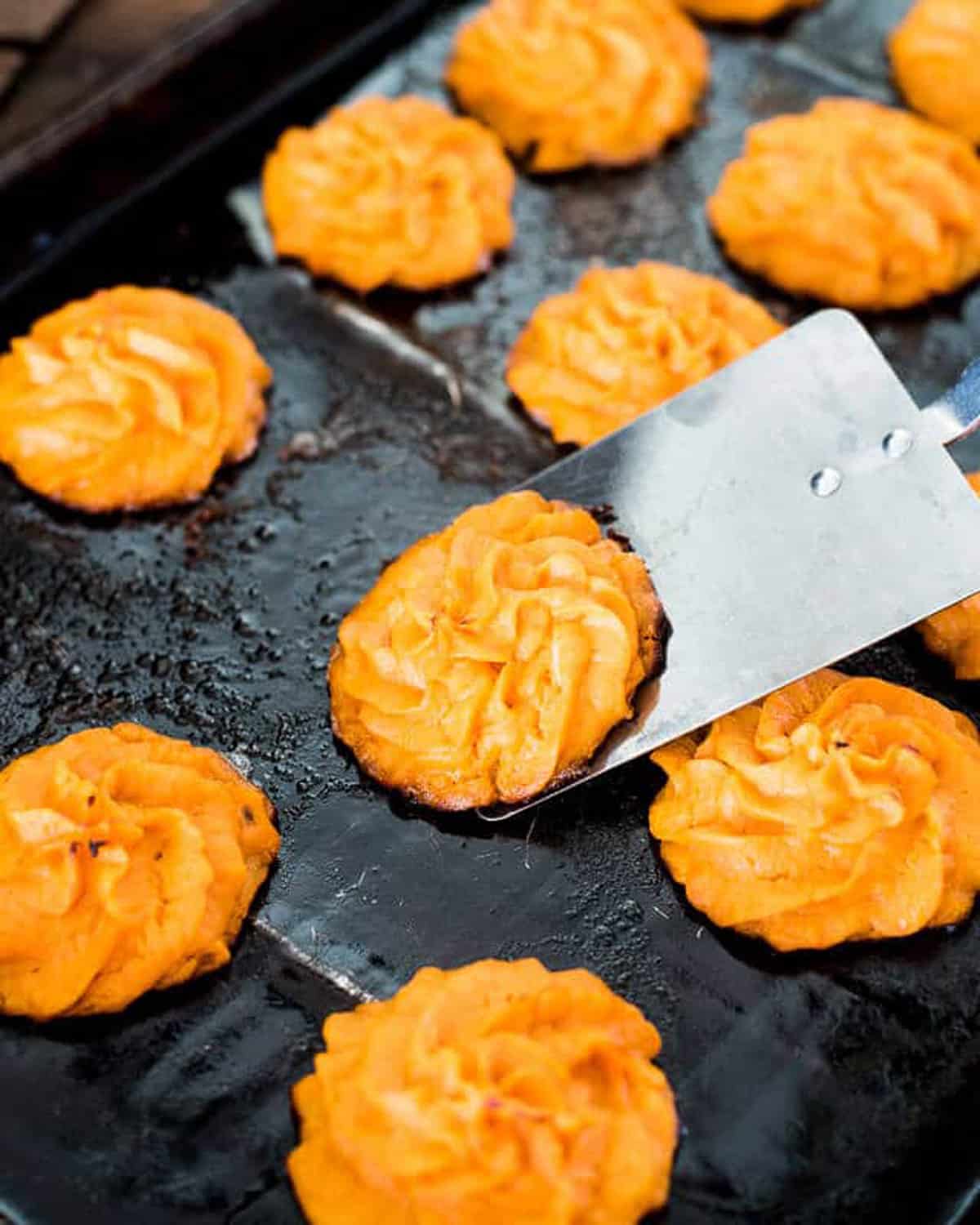 a spatula scooping a sweet potato puff off a baking sheet