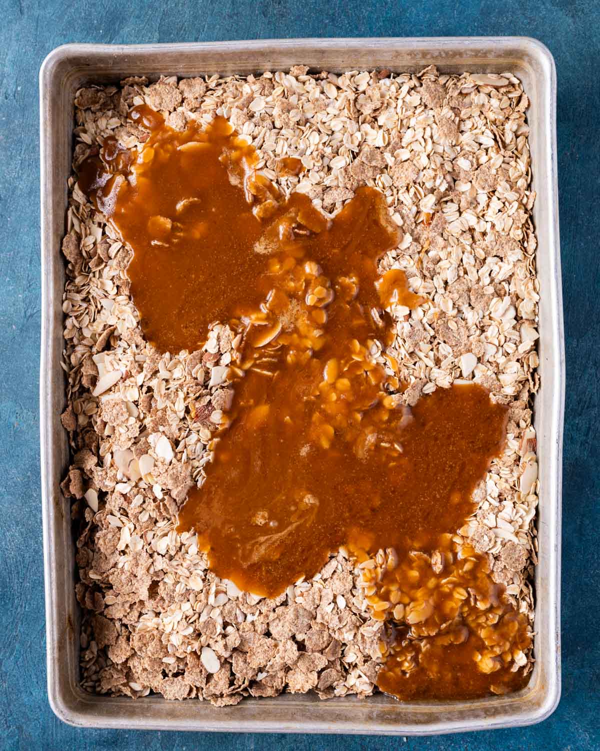 syrup poured over granola ingredients in a baking pan