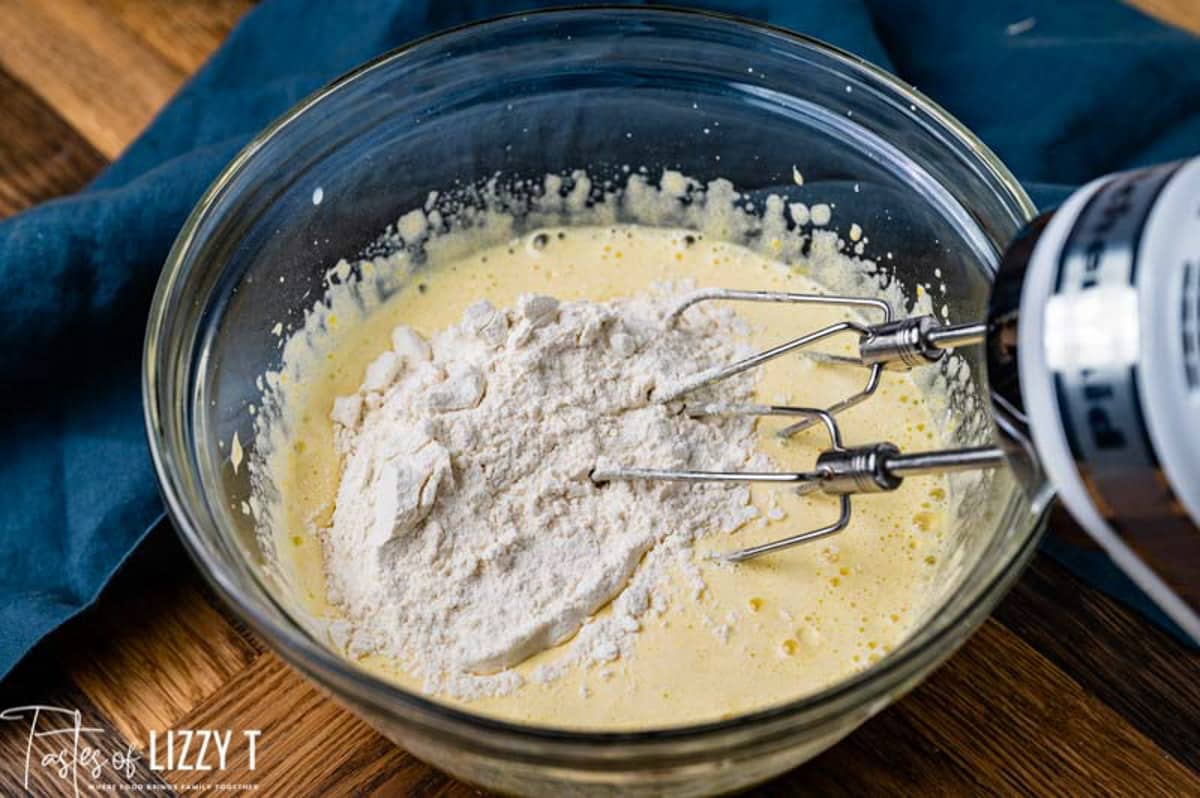 flour over cake batter in a mixing bowl