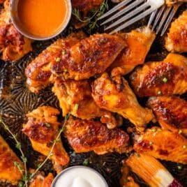 closeup of buffalo wings on a pan with forks and fresh herbs