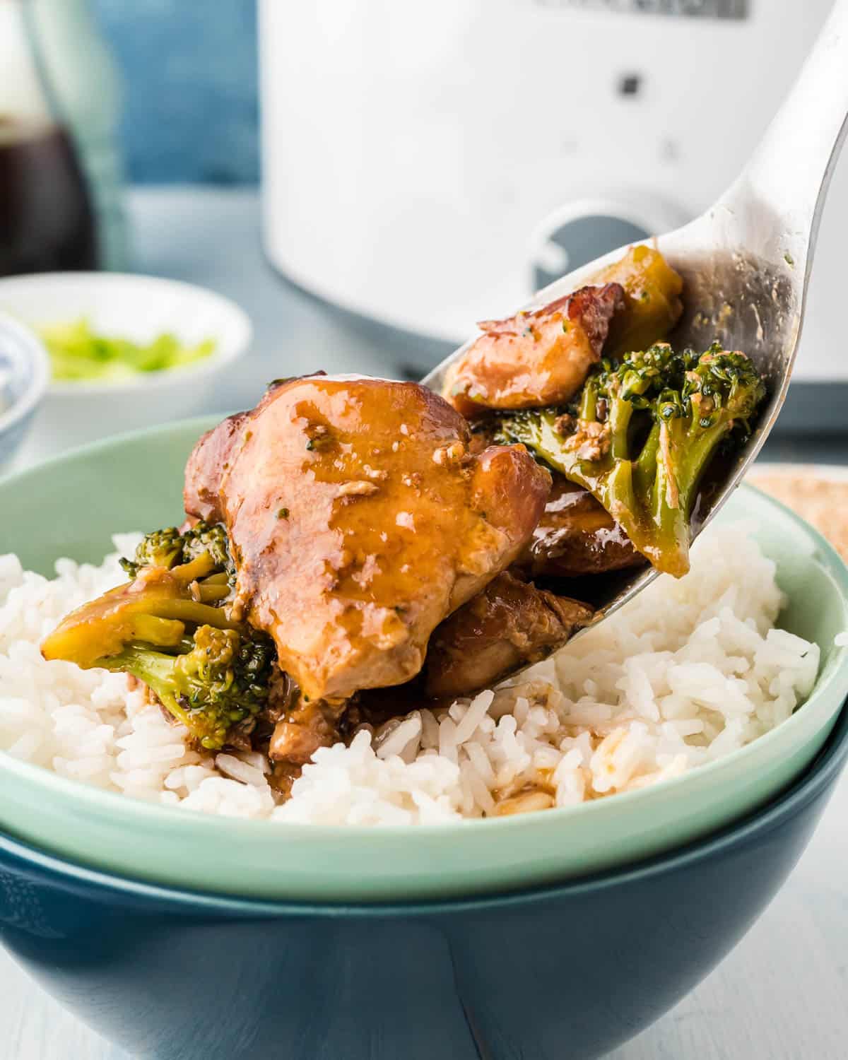 spooning broccoli chicken over rice in a bowl