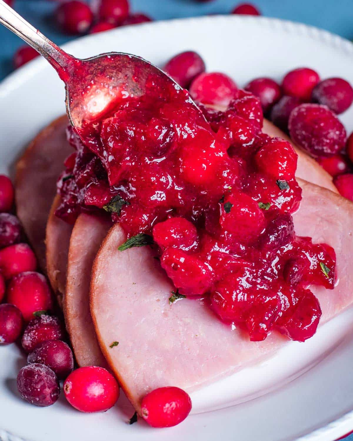 spooning cranberry sauce over ham