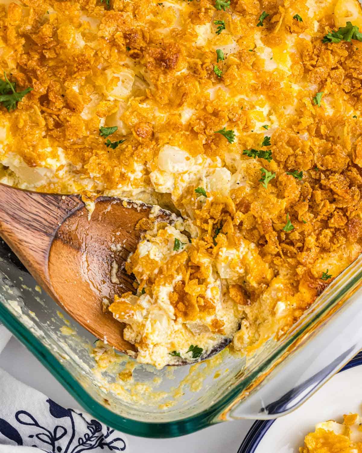 closeup of funeral potatoes in a casserole dish with a wooden spoon