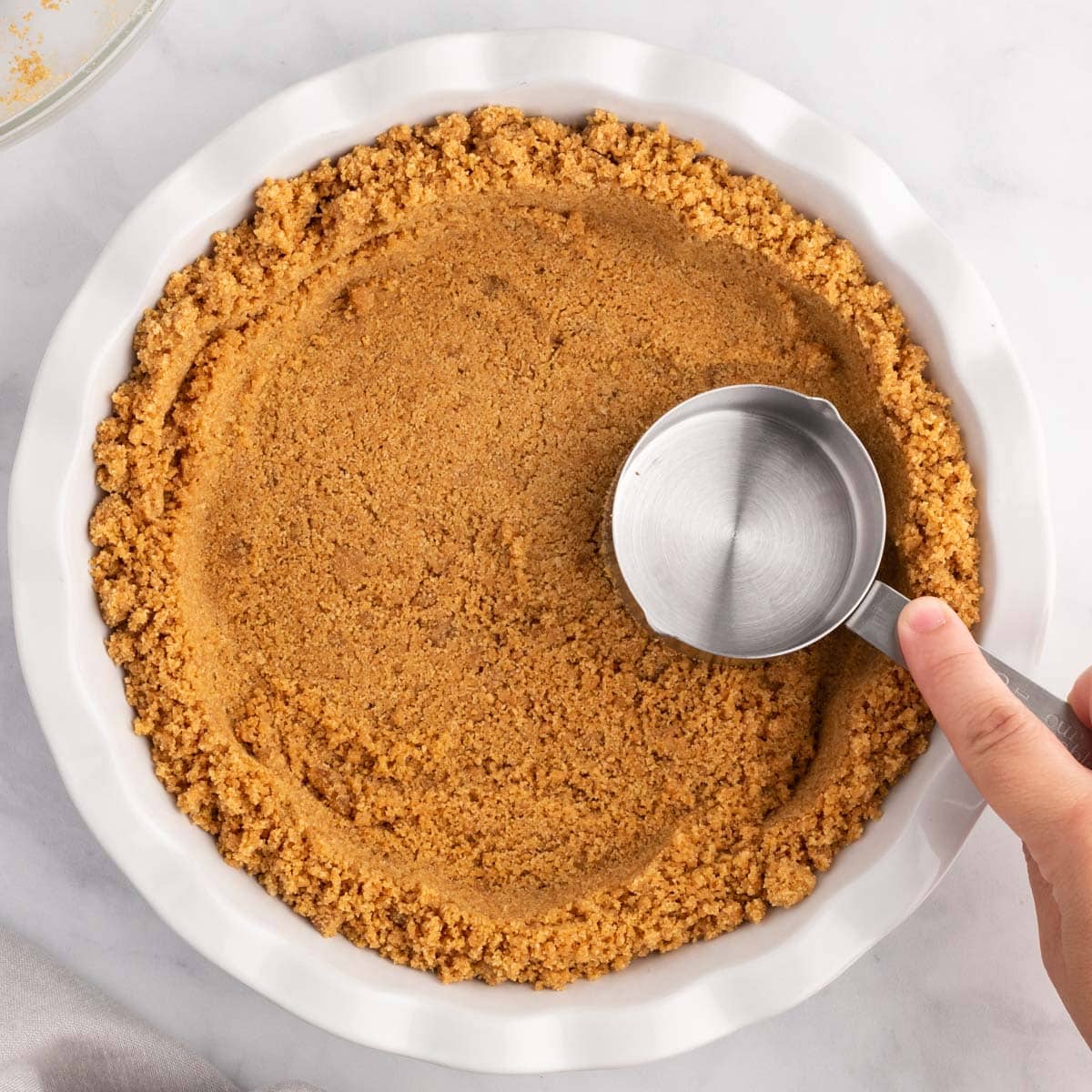 pressing graham cracker crumbs in a pie plate