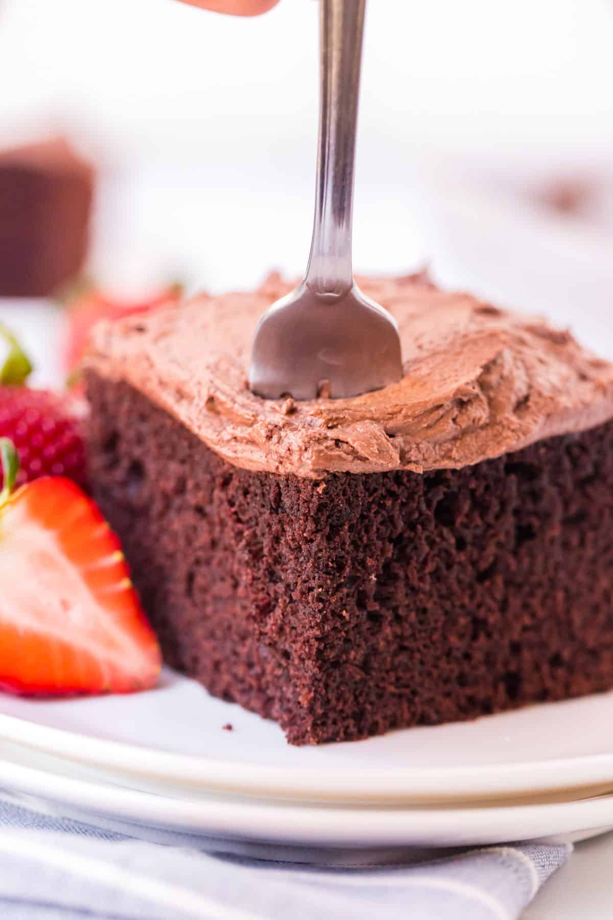 a piece of frosted chocolate cake with a fork in it