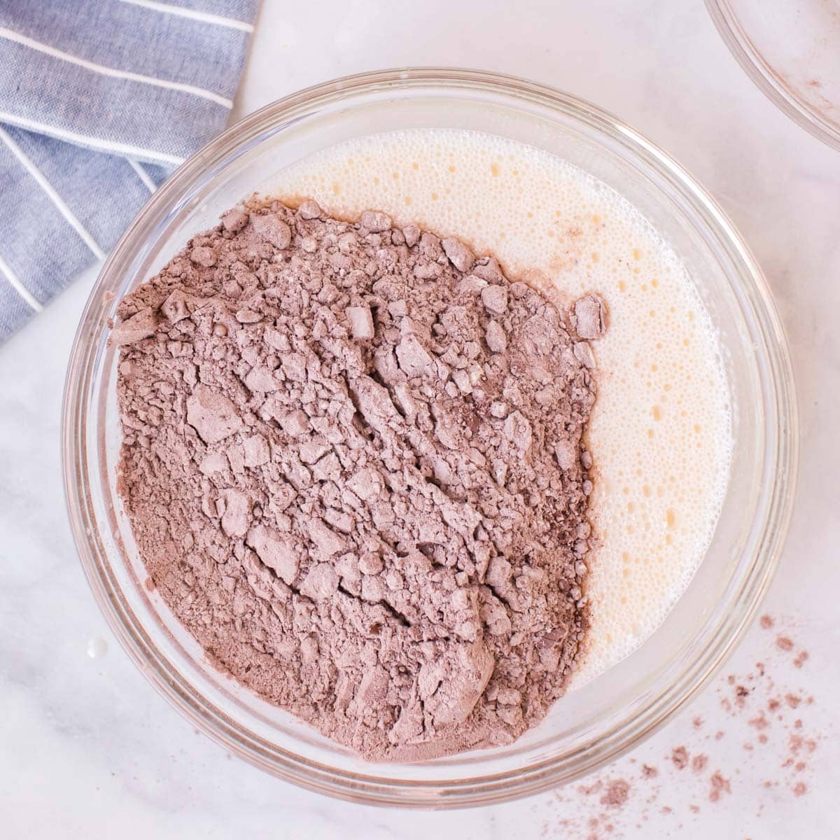 adding dry ingredients to wet ingredients for cake in a glass bowl