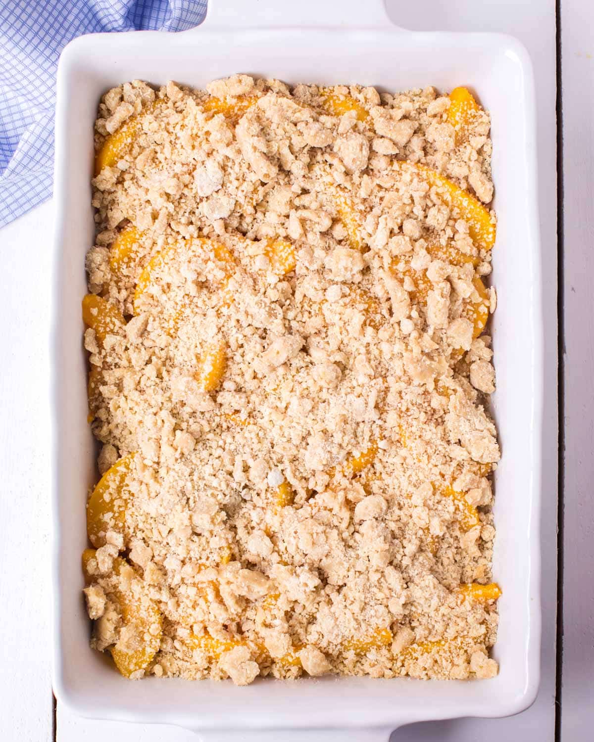 crumb topping sprinkled over peaches in a baking pan