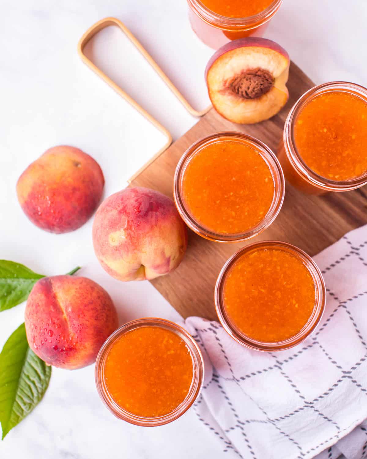 overhead view of peach jam in jars on a table with fresh peaches