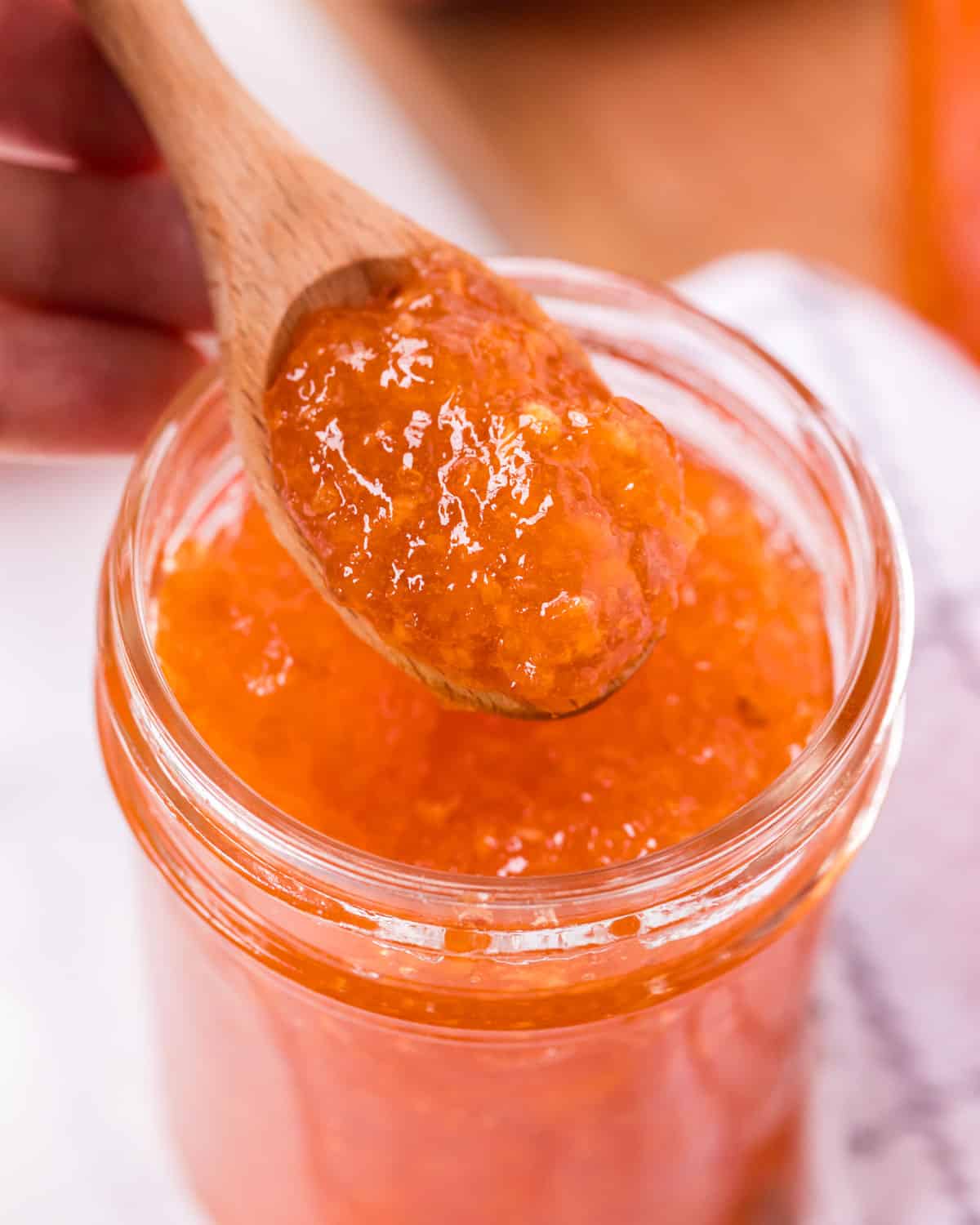 a spoon spooning out peach jam from a jar