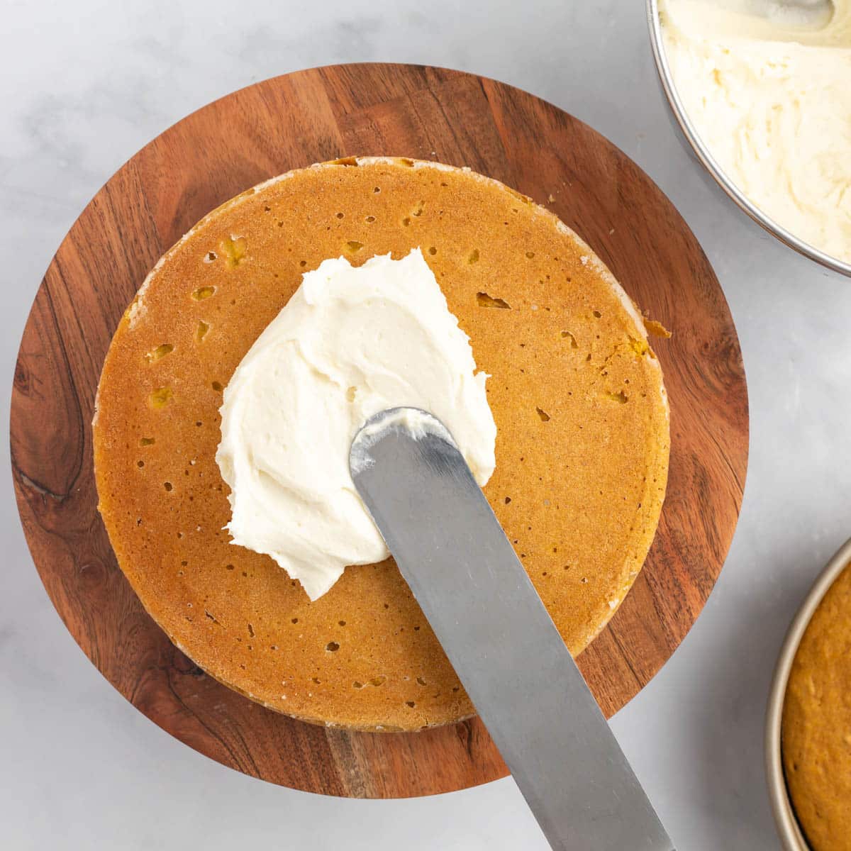 spreading cream cheese frosting on a pumpkin spice cake