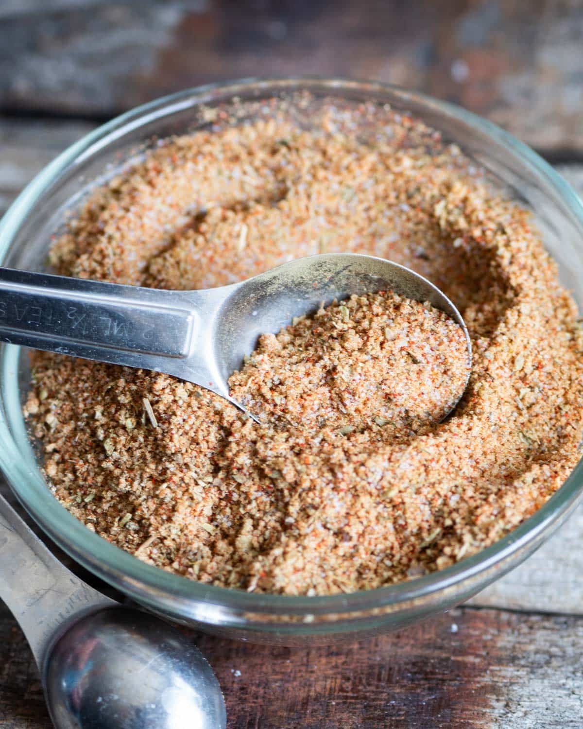 a spice rub in a glass bowl with a teaspoon