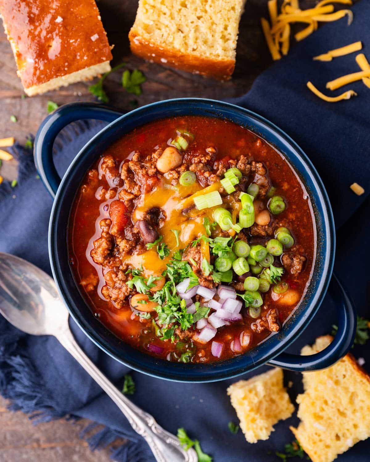 a bowl of sweet chili on a table with cornbread and a spoon