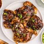 teriyaki chicken thighs on a plate with sesame seeds and green onions