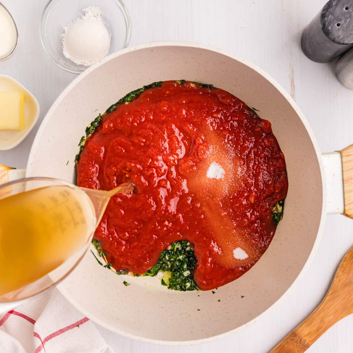 pouring chicken broth in a saucepan with tomatoes