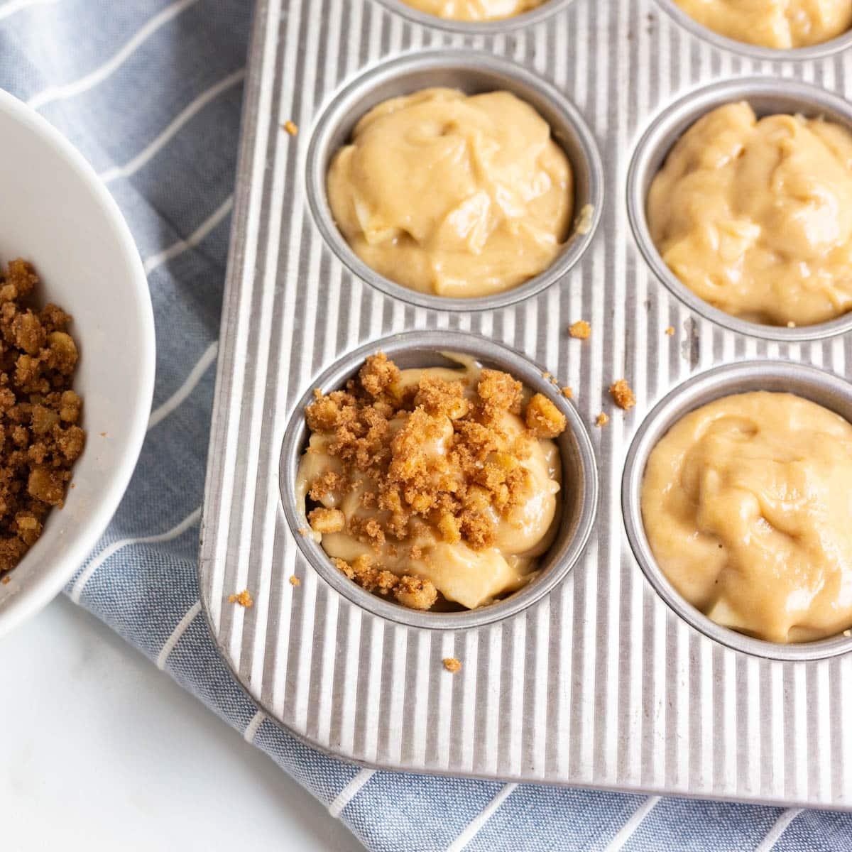 streusel over apple batter in a muffin pan