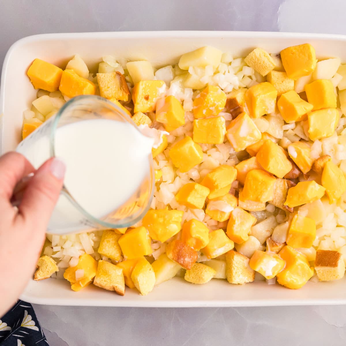 pouring milk over a potato and cheese casserole