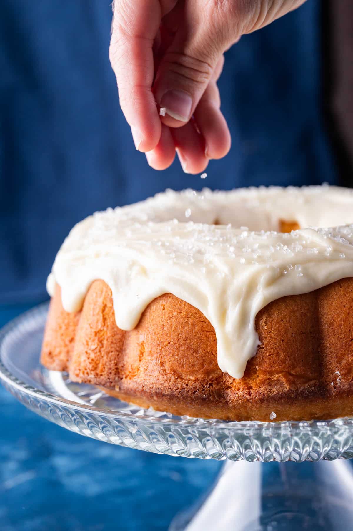 a hand sprinkling sprinkles on top of pound cake glaze