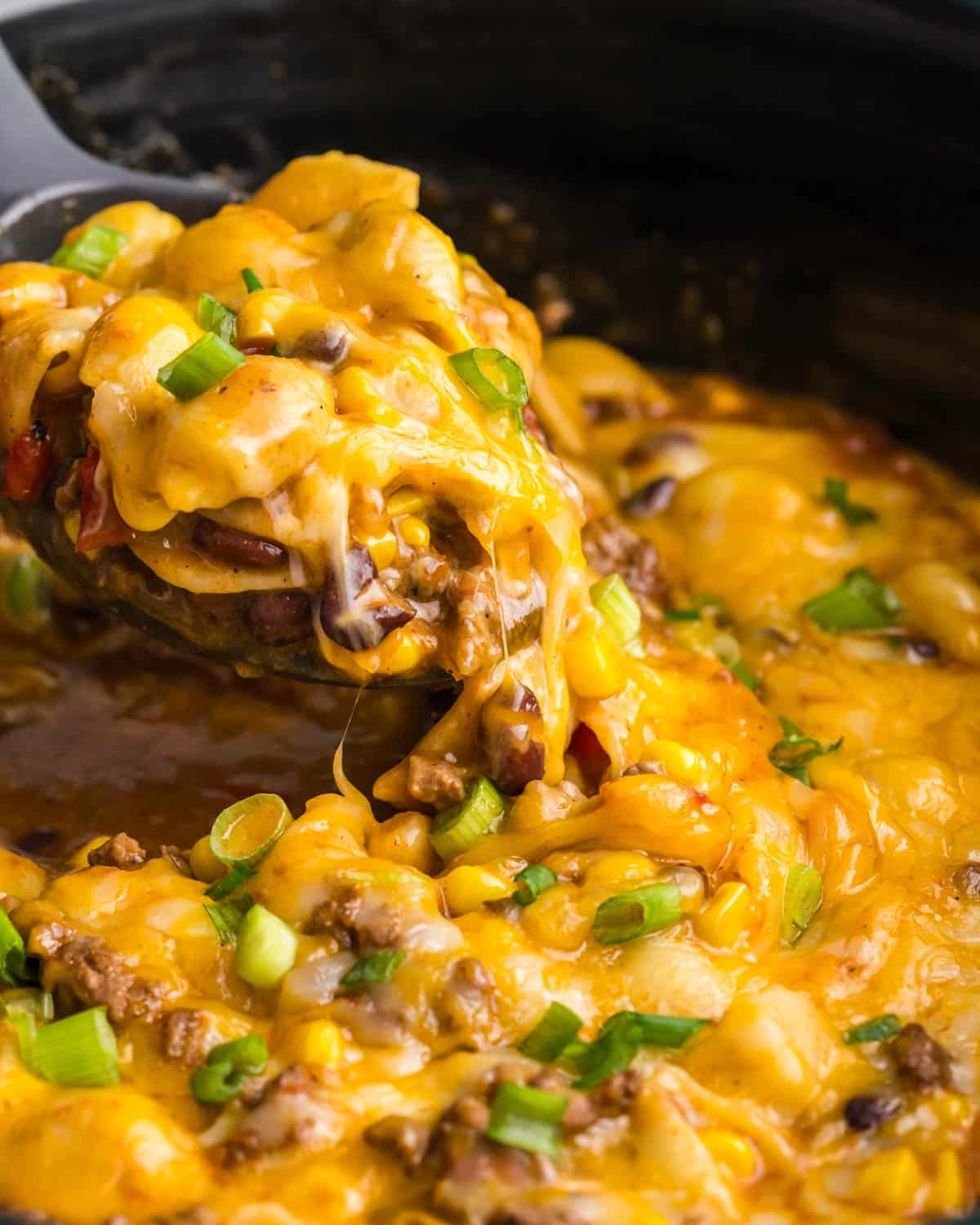 a spoon scooping out cheesy pasta with black beans