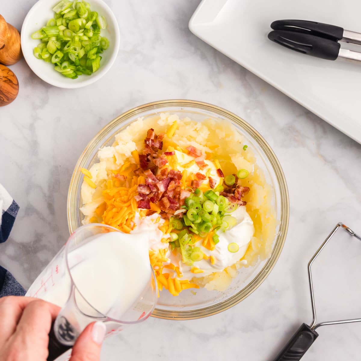 pouring milk over loaded potato fillings in a bowl