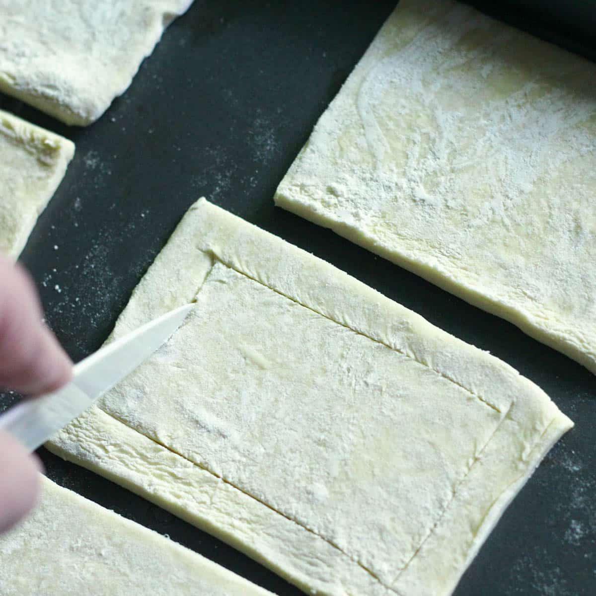 using a knife to score puff pastry on a baking sheet