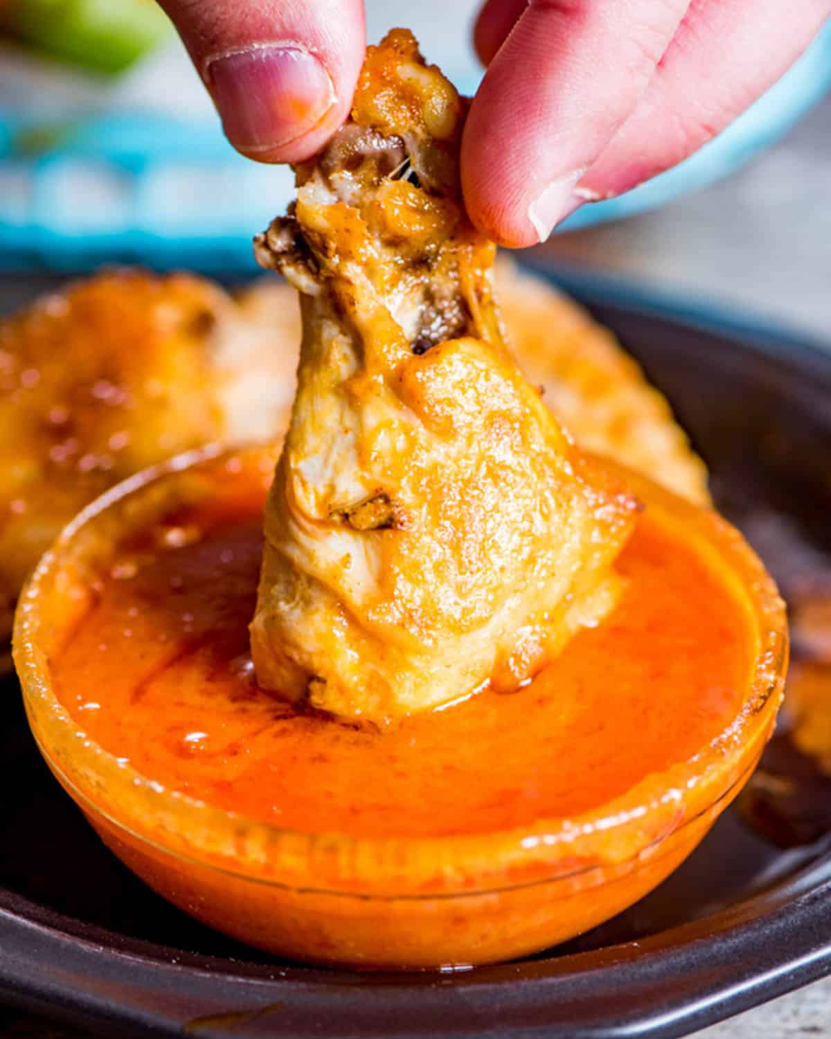 a hand dipping a buffalo wing in buffalo sauce