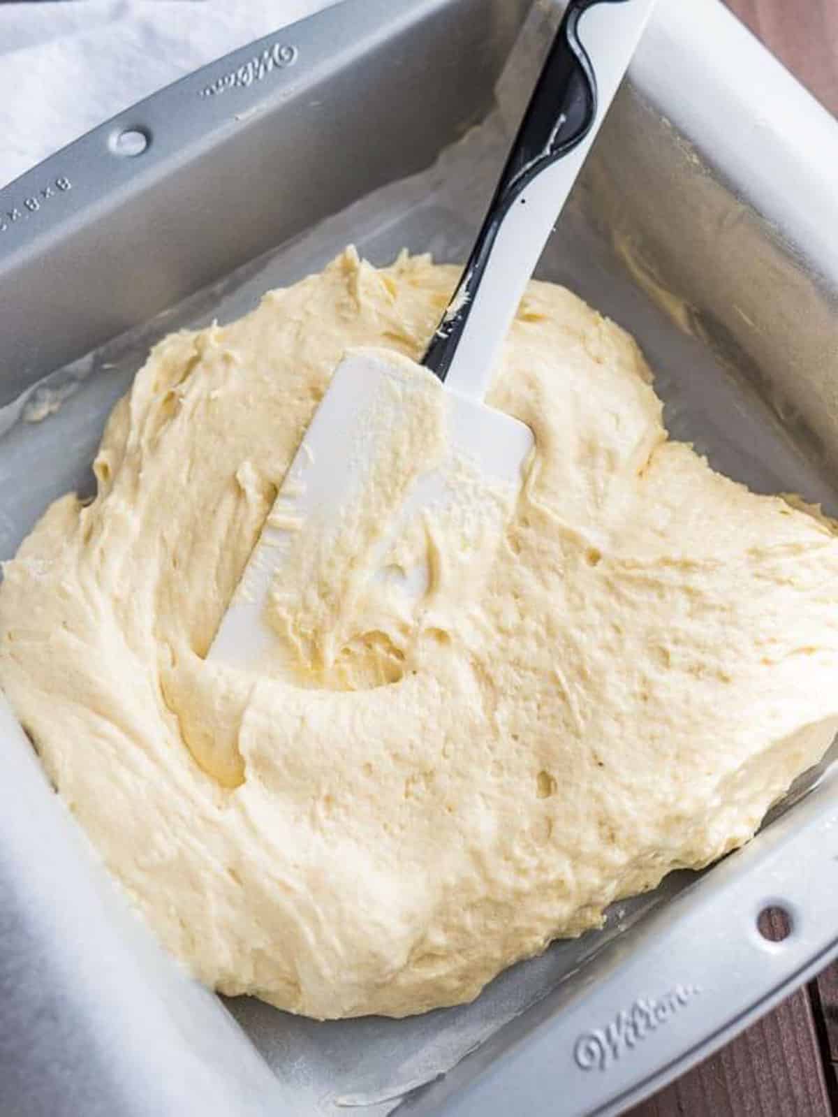 a spatula spreading cake batter in an 8x8" pan