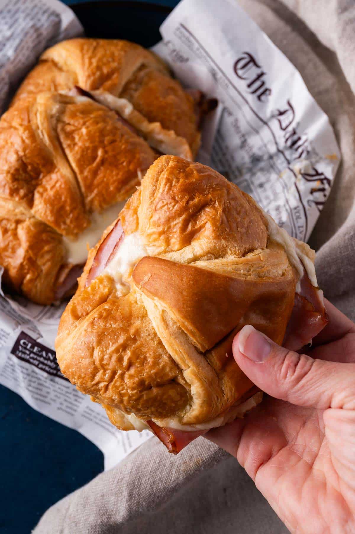 a hand holding a baked croissant sandwich