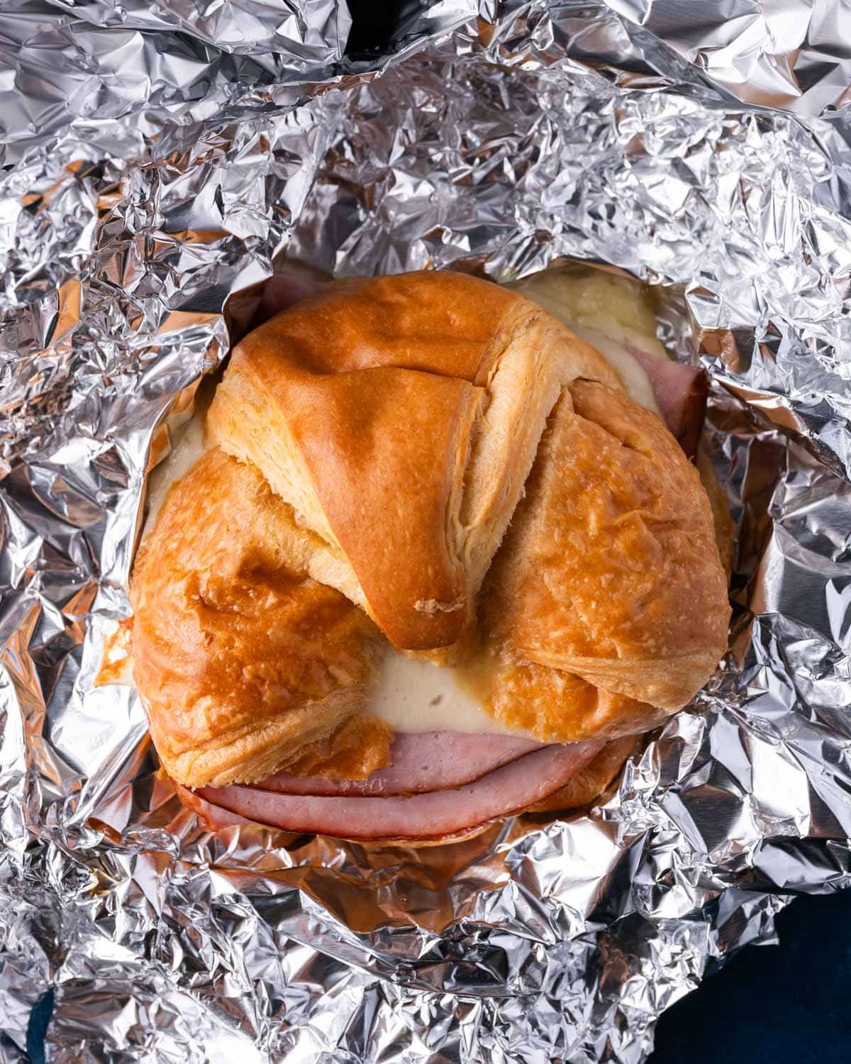 a baked croissant sandwich with ham and cheese in foil