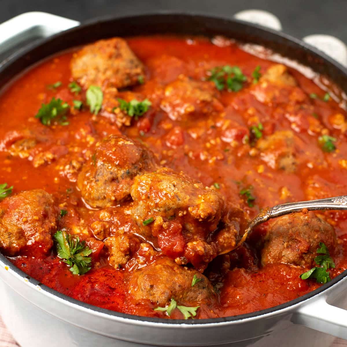 a pan of meatballs with one on a spoon