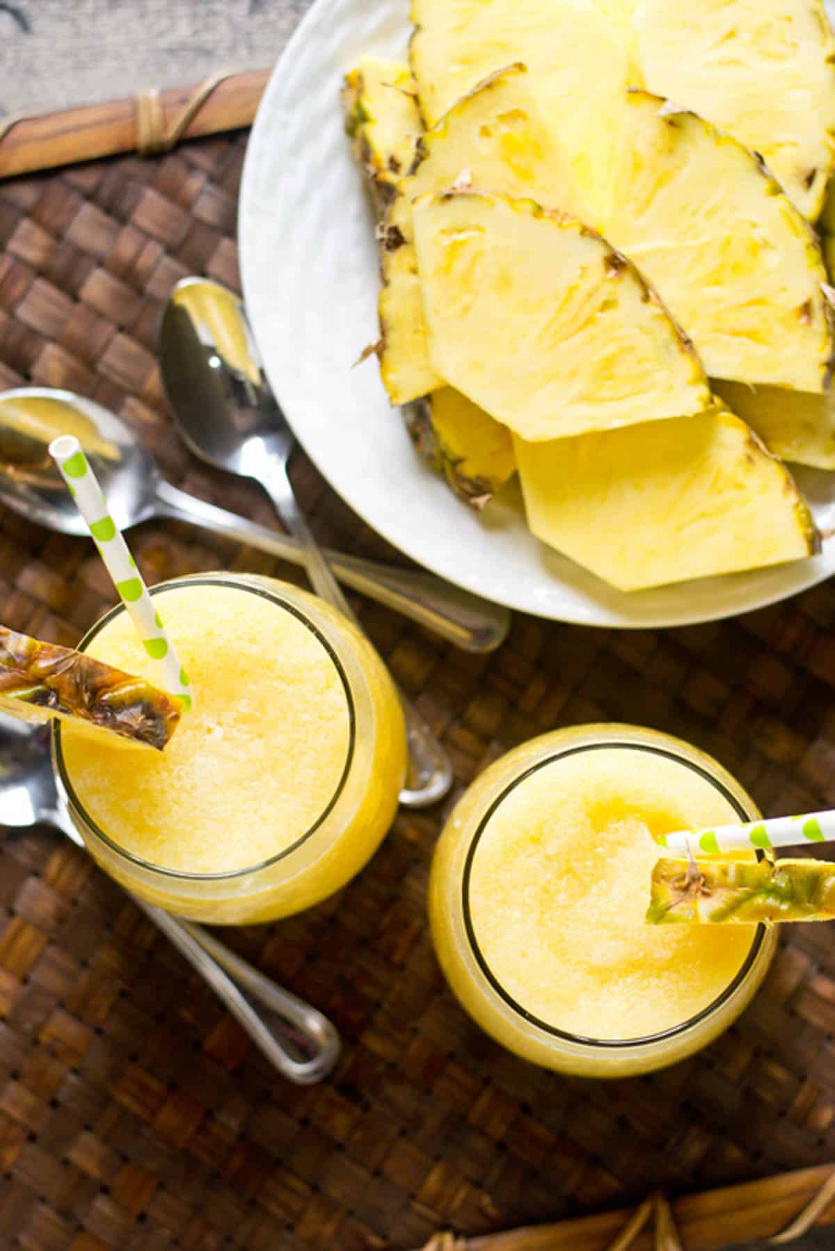 overhead view of two pineapple cream smoothies and a plate of pineapple