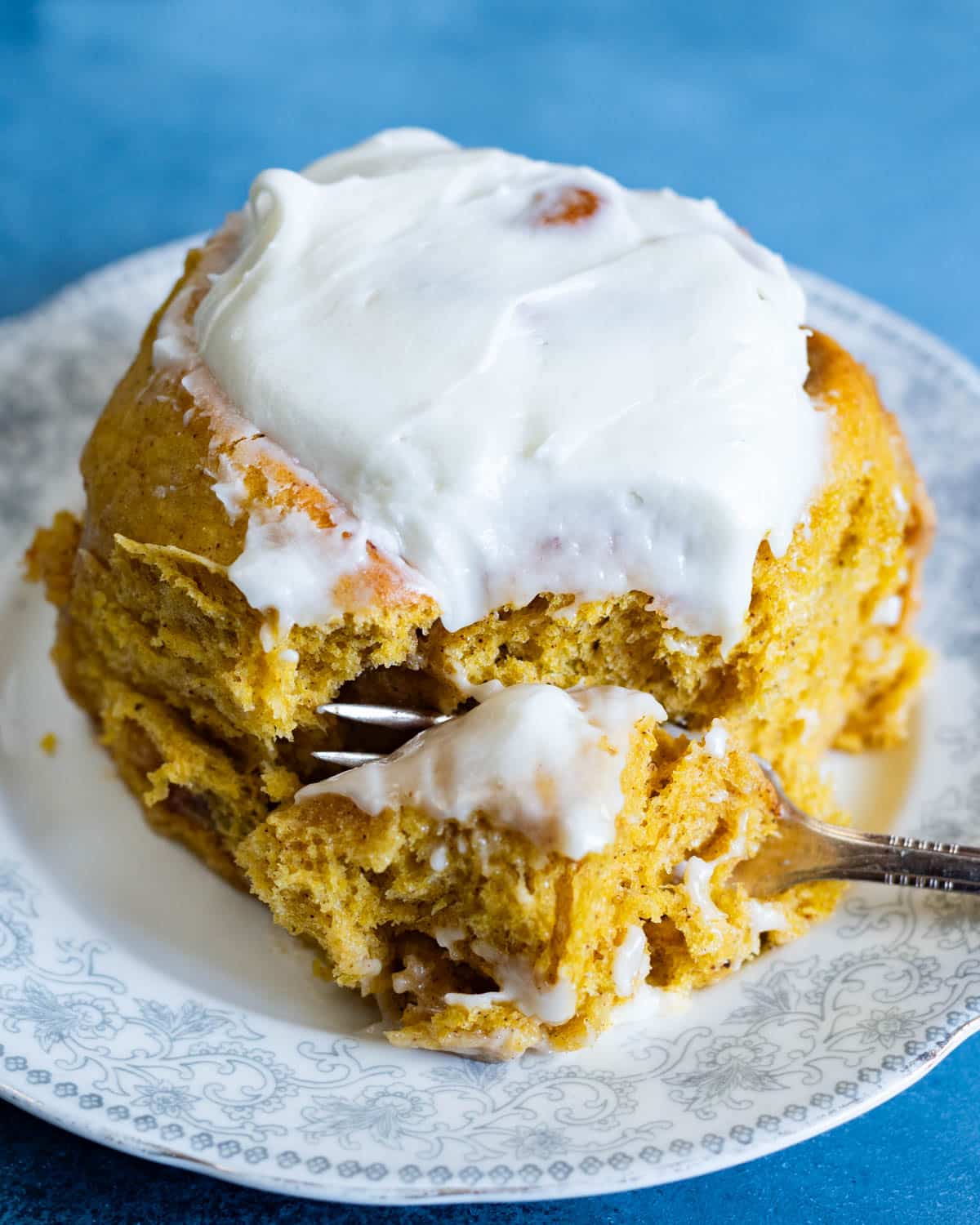 a pumpkin spice cinnamon roll on a plate with a fork