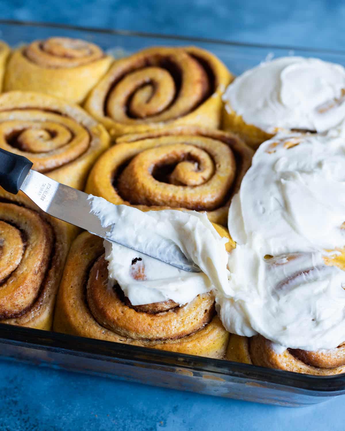 spreading cream cheese frosting on pumpkin rolls