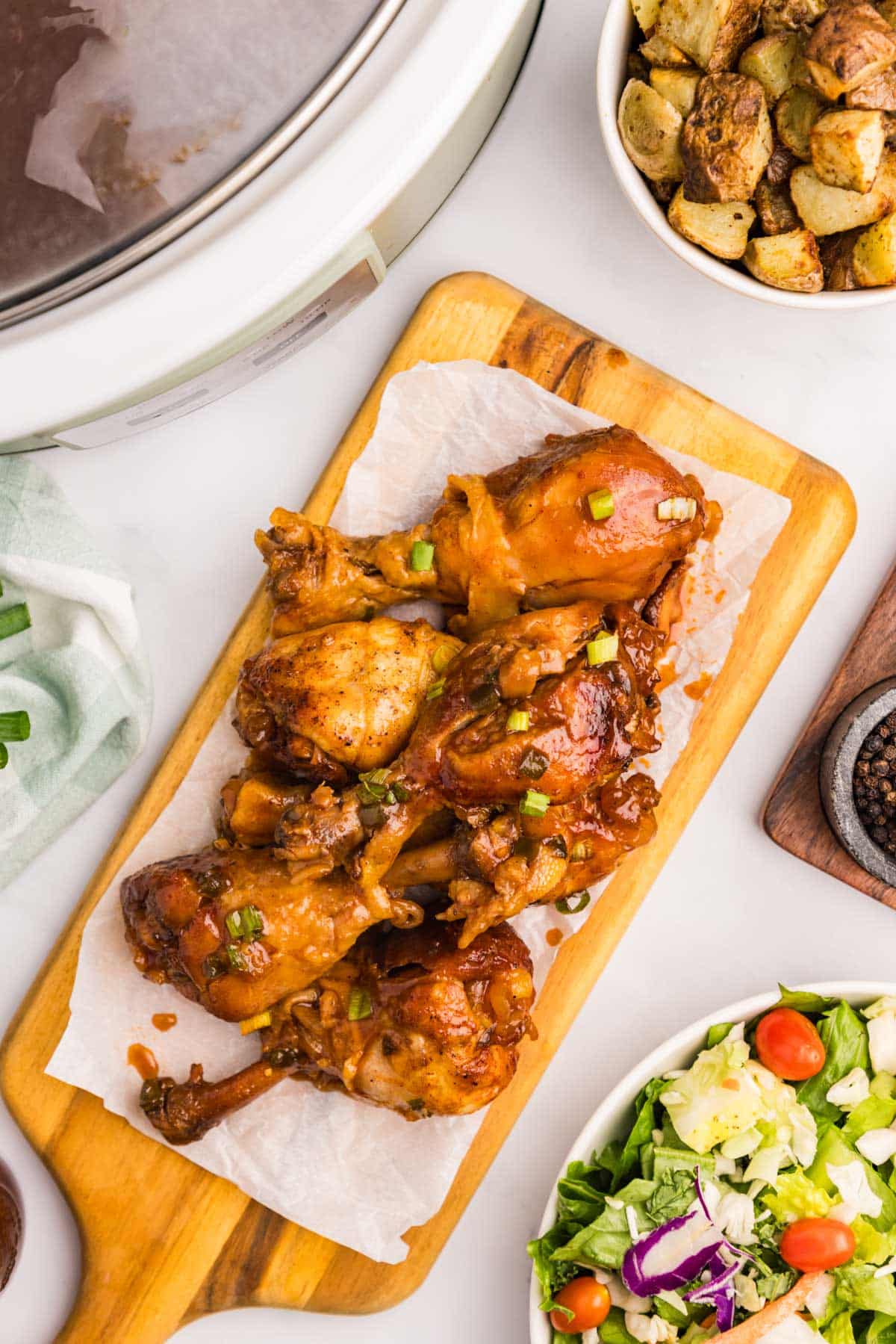 chicken drumsticks on a table with potatoes and salad