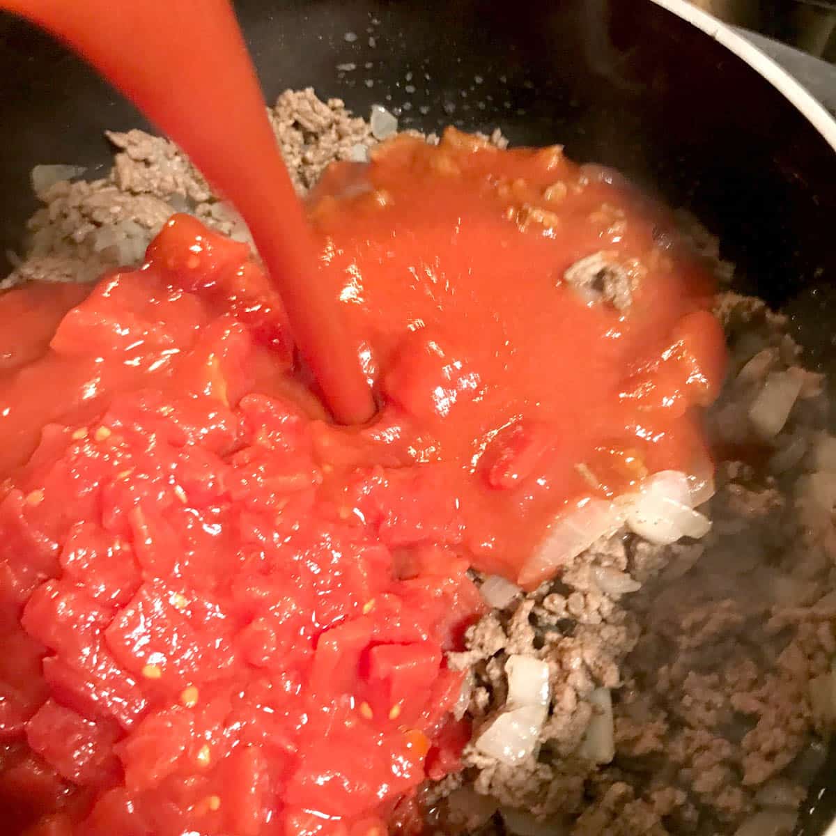 pouring tomato sauce into a skillet