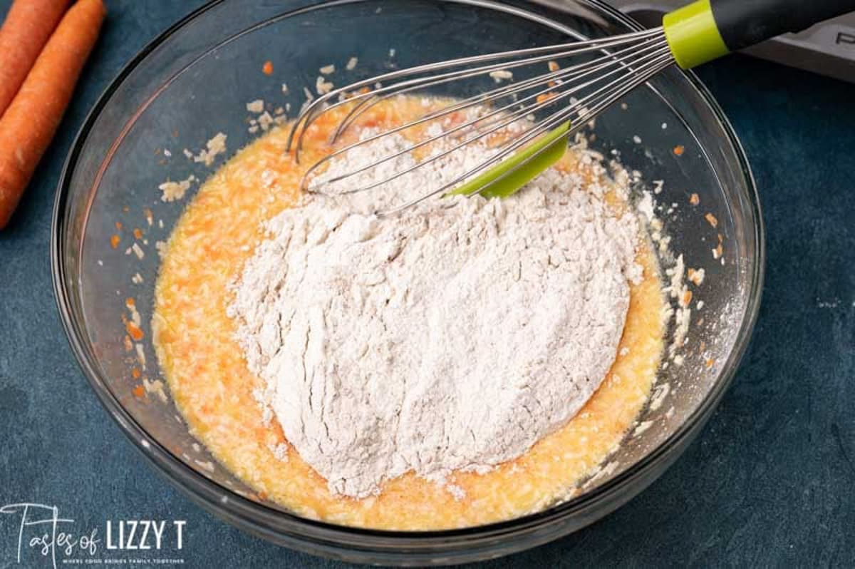 flour over wet ingredients in a bowl with a whisk